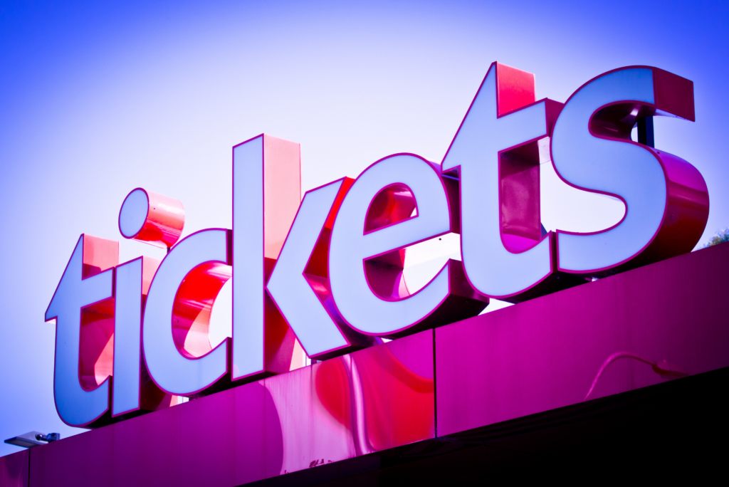 A large red and white sign that says "Tickets", in front of a blue sky.