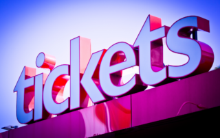 A large red and white sign that says "Tickets", in front of a blue sky.