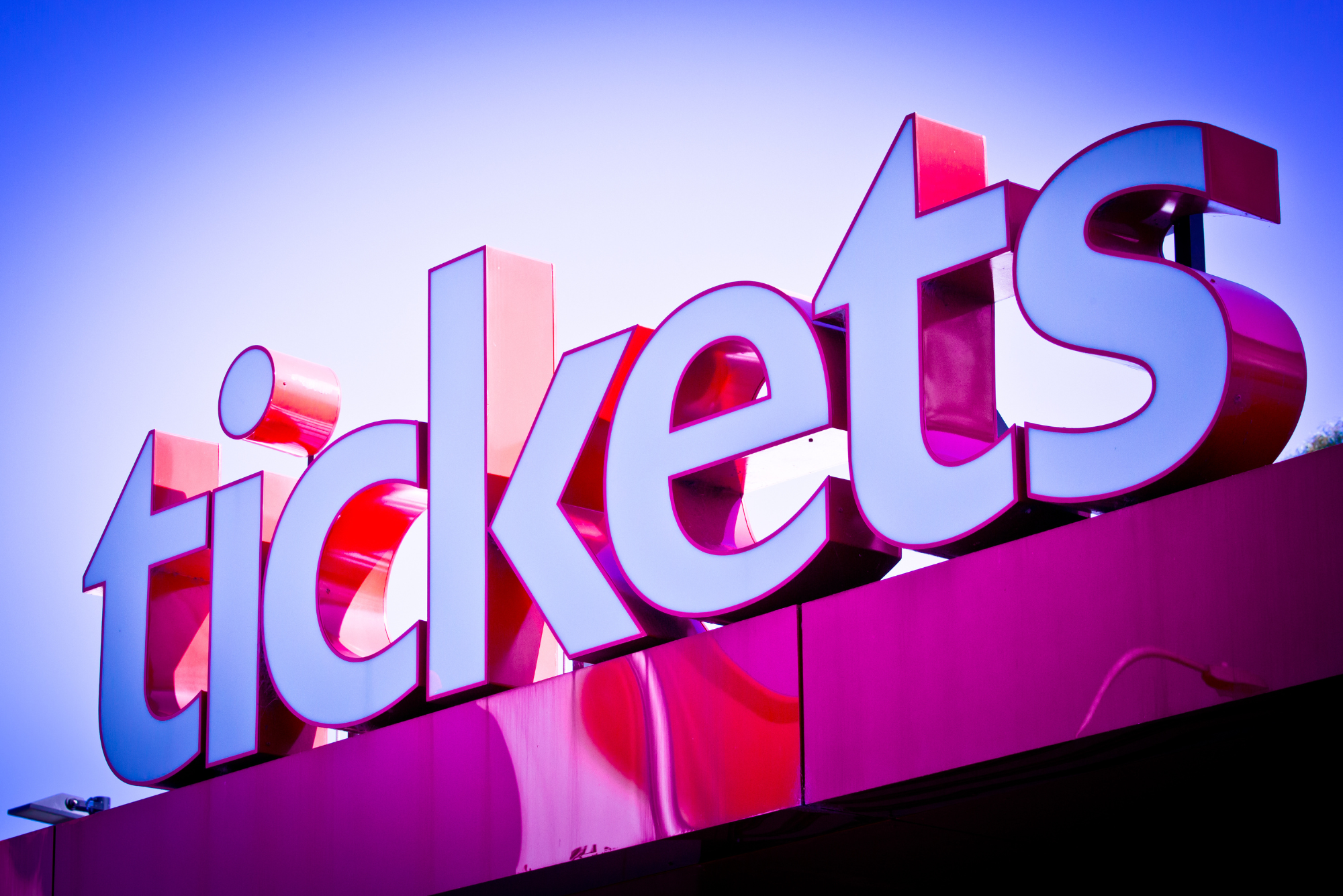 A large red and white sign that says "Tickets", in front of a blue sky.
