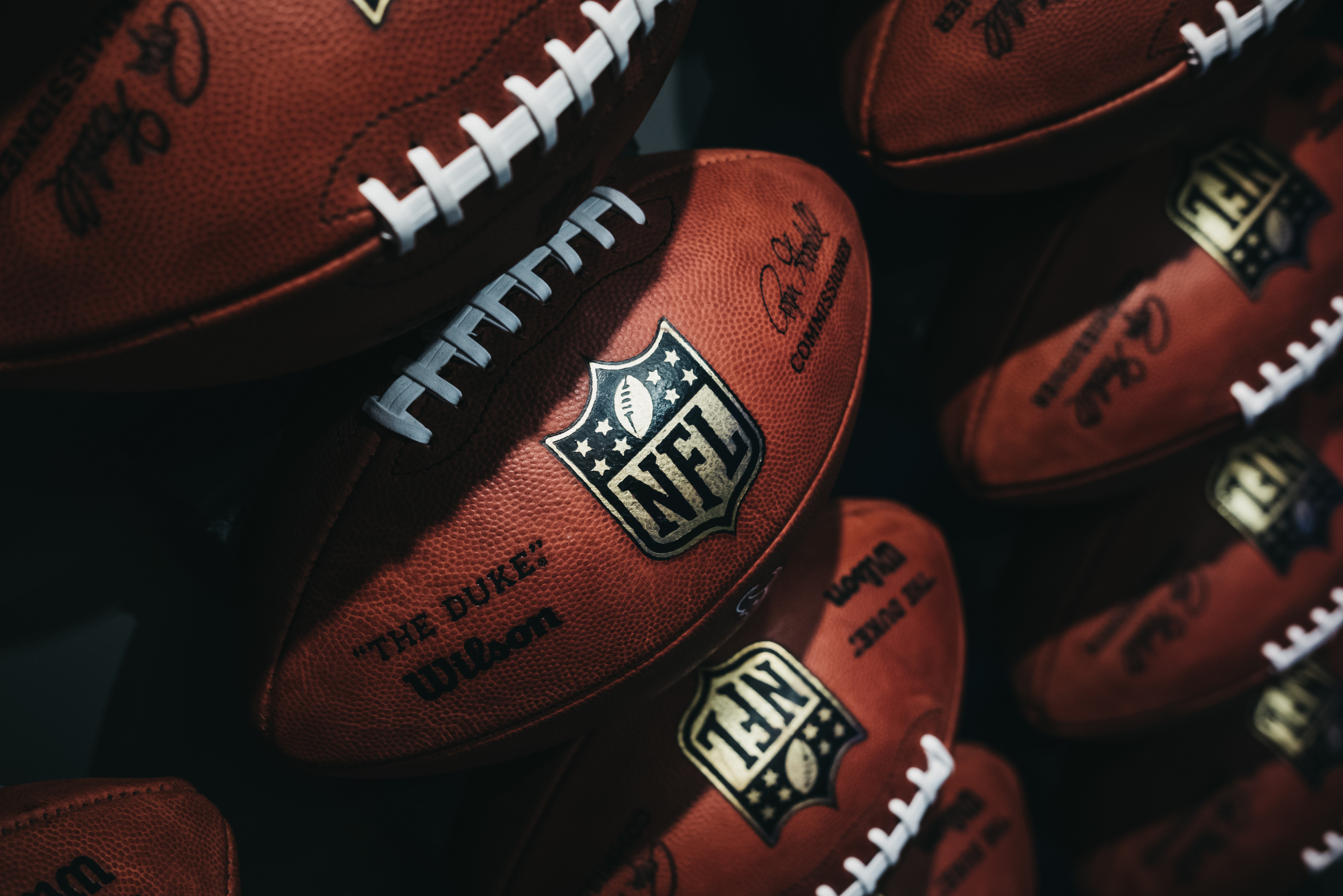 A bunch of official NFL game balls are piled up, representing how sports teams are dropping the ball when it comes to ticket sales.