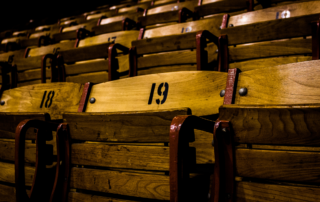 A close-up view of many rows of old wooden stadium seats with painted numbers and red trim.