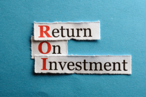 The words “Return on Investment” on small strips of paper, with the first letter in red ink, lie on a teal blue background.