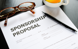 A sponsorship proposal rests on a desk by a pair of glasses, mug, and a black ballpoint pen.
